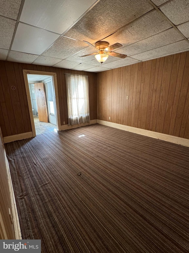 unfurnished room with wood walls, a paneled ceiling, and ceiling fan