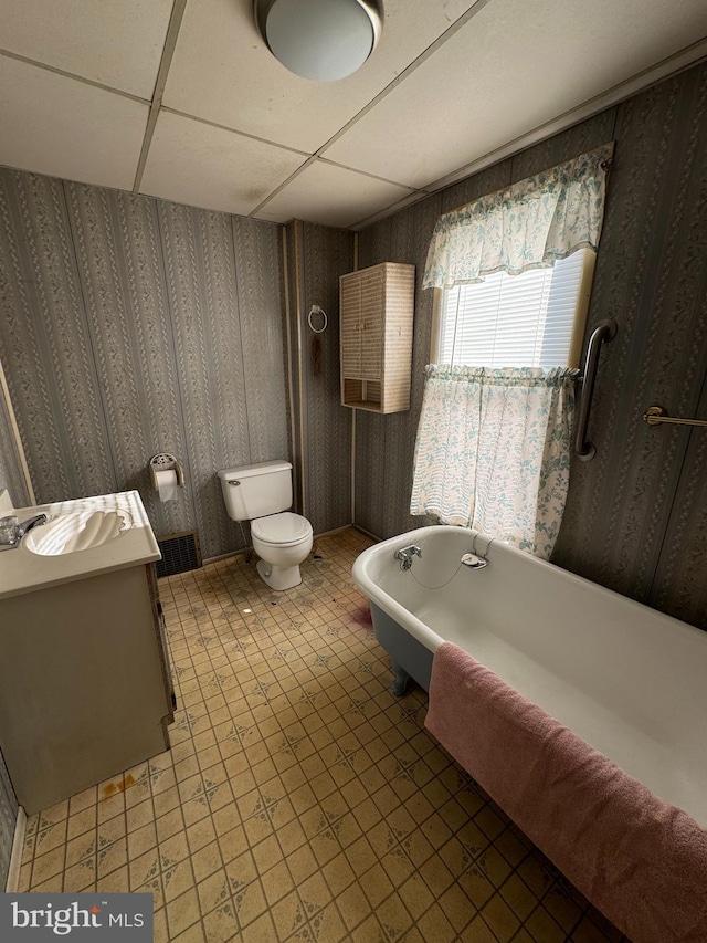 bathroom with vanity, a tub, tile patterned flooring, toilet, and a drop ceiling