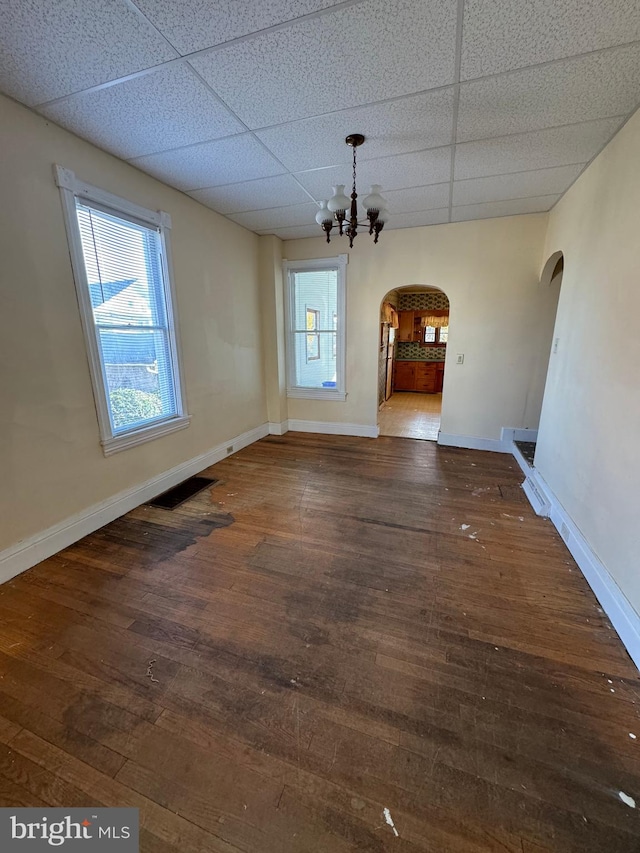 unfurnished dining area with dark hardwood / wood-style flooring, a paneled ceiling, and a chandelier