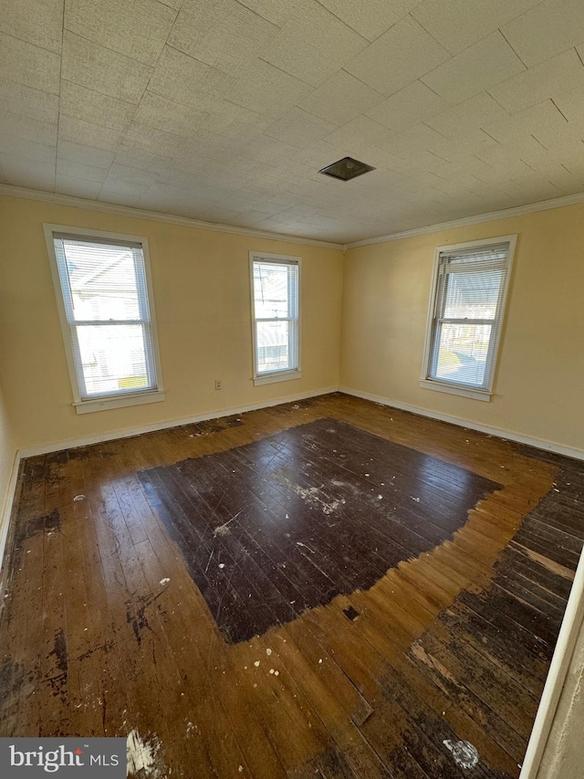 empty room with dark wood-type flooring, a wealth of natural light, and ornamental molding