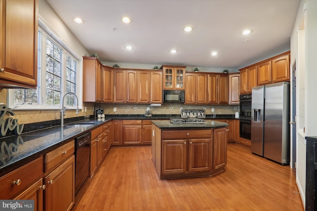 kitchen featuring sink, light hardwood / wood-style flooring, dark stone counters, a kitchen island, and black appliances