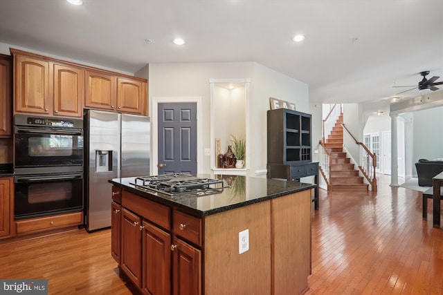 kitchen with ceiling fan, a center island, stainless steel appliances, dark stone counters, and light wood-type flooring