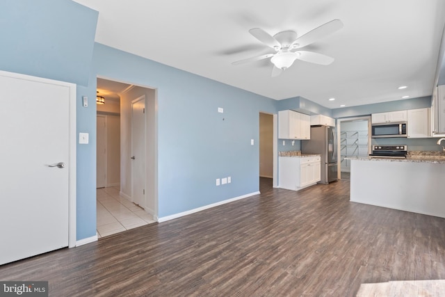 kitchen with stainless steel appliances, white cabinets, hardwood / wood-style floors, ceiling fan, and light stone countertops