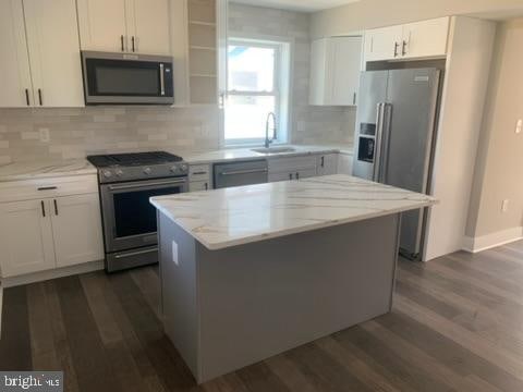 kitchen featuring white cabinetry, appliances with stainless steel finishes, light stone countertops, a kitchen island, and dark wood-type flooring