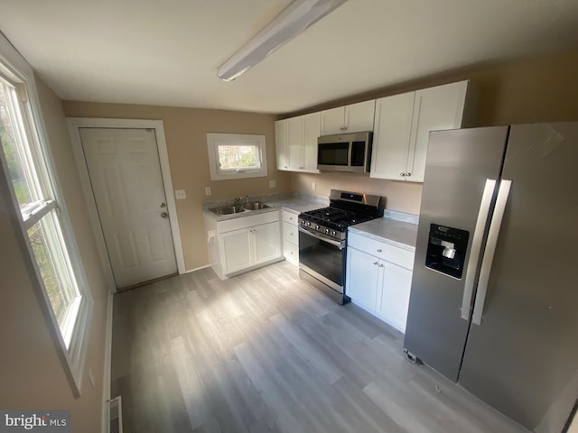 kitchen with stainless steel appliances, white cabinetry, and light wood-type flooring