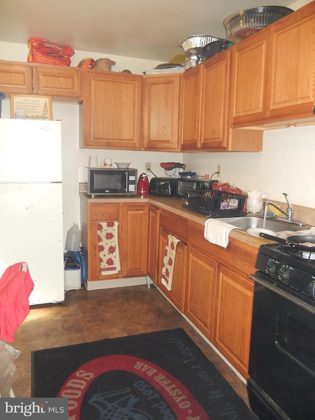 215 Concord Ave, Wilmington, DE 19802 - kitchen featuring black range with gas stovetop, freestanding refrigerator, a sink, dark tile patterned floors, and brown cabinets