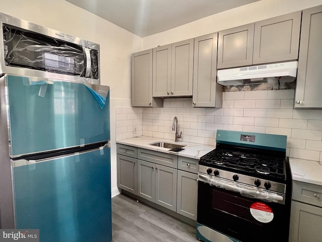 kitchen featuring gray cabinetry, light stone counters, stainless steel appliances, sink, and light hardwood / wood-style floors