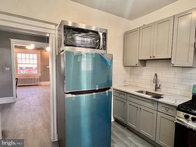 kitchen featuring sink, wood-type flooring, radiator heating unit, and appliances with stainless steel finishes