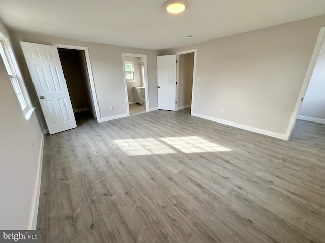 unfurnished bedroom with ensuite bathroom and light wood-type flooring