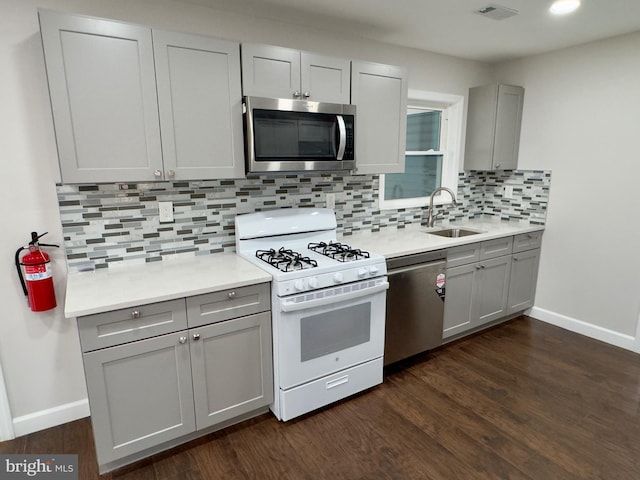 kitchen with gray cabinetry, sink, stainless steel appliances, dark hardwood / wood-style floors, and decorative backsplash