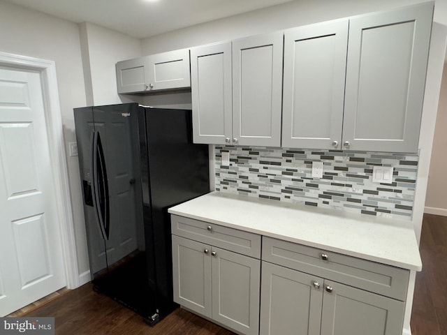 kitchen with tasteful backsplash, gray cabinetry, black fridge, and dark hardwood / wood-style floors