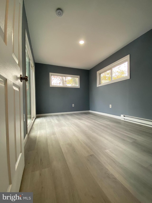 spare room featuring a wealth of natural light, a baseboard heating unit, and light hardwood / wood-style floors