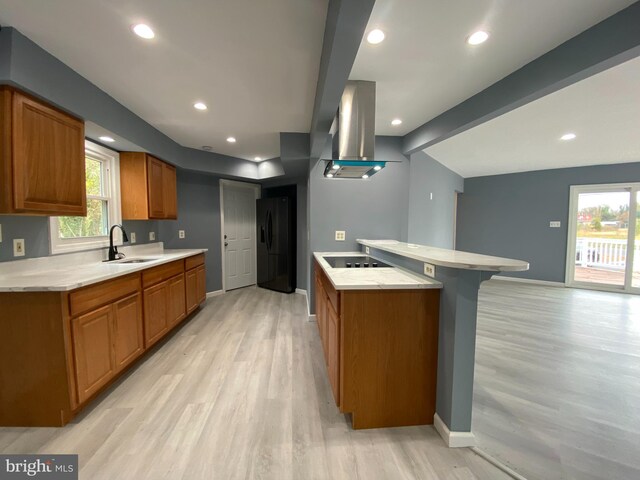 kitchen with black appliances, range hood, sink, a kitchen breakfast bar, and light hardwood / wood-style flooring