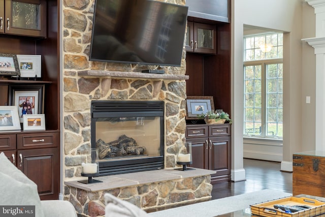 living room with a stone fireplace, dark hardwood / wood-style flooring, and plenty of natural light