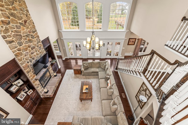 living room featuring a stone fireplace, a towering ceiling, dark wood-type flooring, and an inviting chandelier