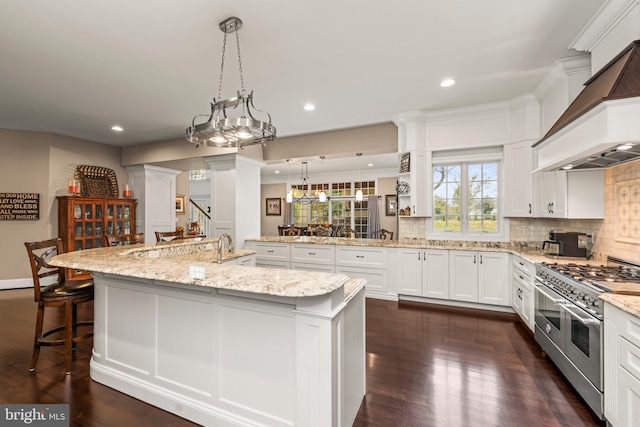 kitchen with a large island with sink, dark hardwood / wood-style floors, an inviting chandelier, range with two ovens, and custom exhaust hood