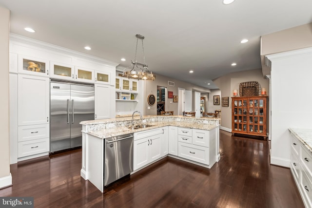 kitchen with white cabinetry, appliances with stainless steel finishes, light stone countertops, decorative light fixtures, and dark wood-type flooring