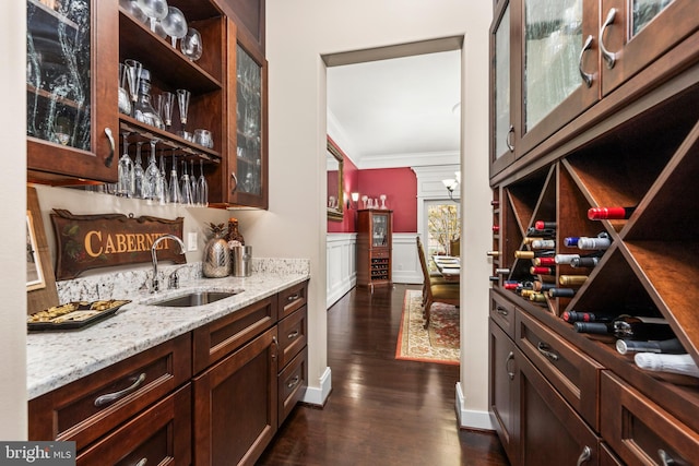 bar with dark wood-type flooring, light stone counters, dark brown cabinetry, sink, and crown molding