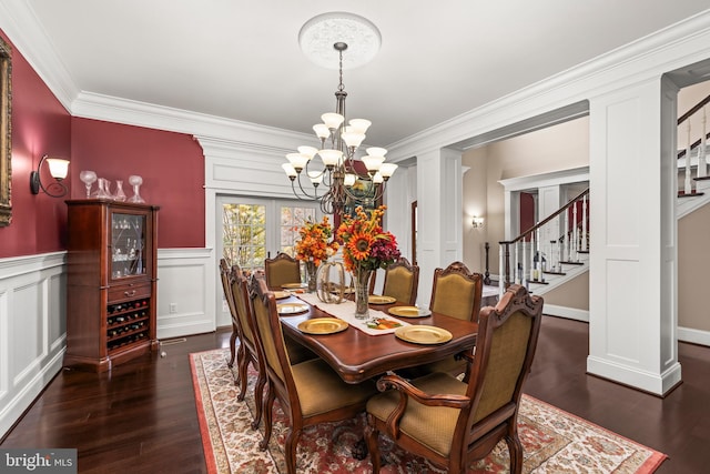 dining space featuring french doors, dark wood-type flooring, a notable chandelier, decorative columns, and ornamental molding