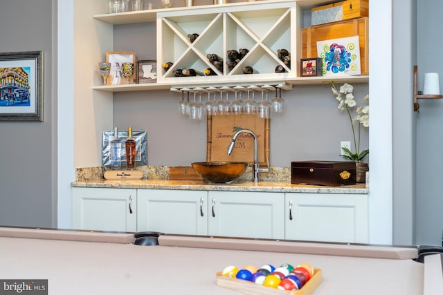 bar featuring light stone countertops, sink, and white cabinets