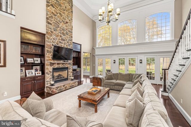 living room with a high ceiling, ornamental molding, a fireplace, wood-type flooring, and a chandelier