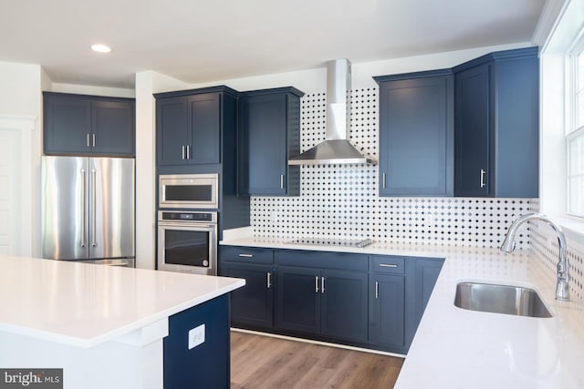 kitchen with stainless steel appliances, sink, wall chimney exhaust hood, blue cabinetry, and light hardwood / wood-style flooring