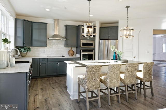 kitchen featuring stainless steel appliances, dark hardwood / wood-style flooring, sink, an island with sink, and wall chimney range hood