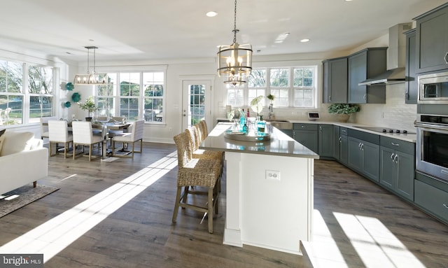 kitchen with stainless steel appliances, dark wood-type flooring, wall chimney exhaust hood, a kitchen island, and decorative light fixtures