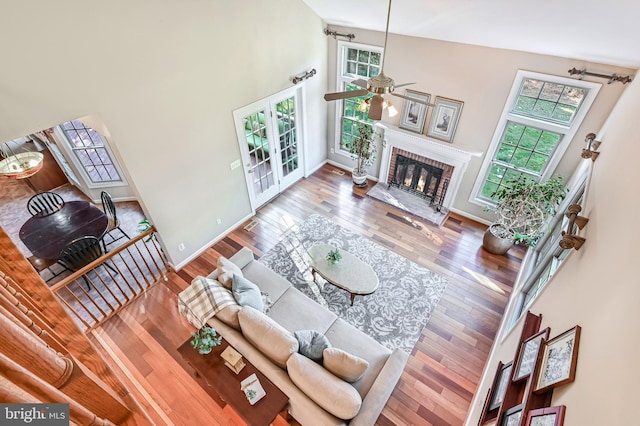 living room with ceiling fan, high vaulted ceiling, wood-type flooring, and a brick fireplace