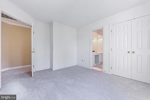 unfurnished bedroom with ensuite bath, a closet, and light colored carpet