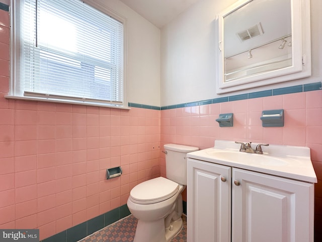 bathroom with tile patterned flooring, vanity, toilet, and tile walls