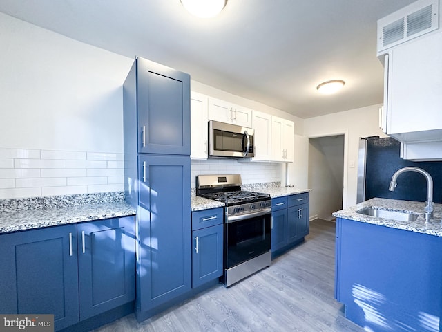 kitchen with blue cabinetry, sink, light hardwood / wood-style floors, white cabinets, and appliances with stainless steel finishes