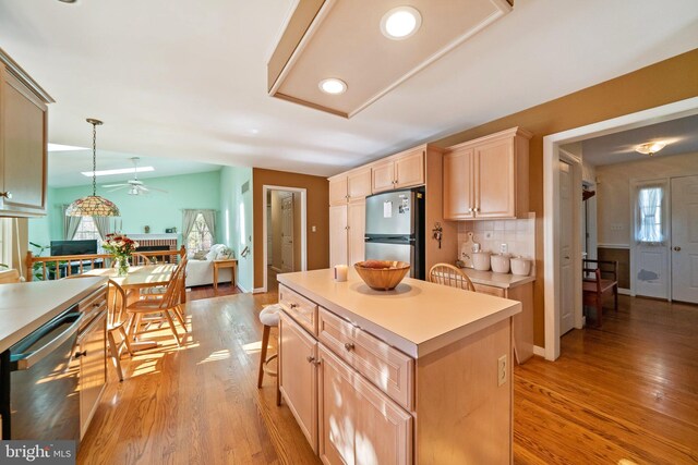 kitchen with stainless steel appliances, a kitchen island, backsplash, decorative light fixtures, and light hardwood / wood-style flooring