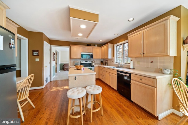 kitchen featuring a kitchen island, light wood-type flooring, appliances with stainless steel finishes, light brown cabinetry, and sink