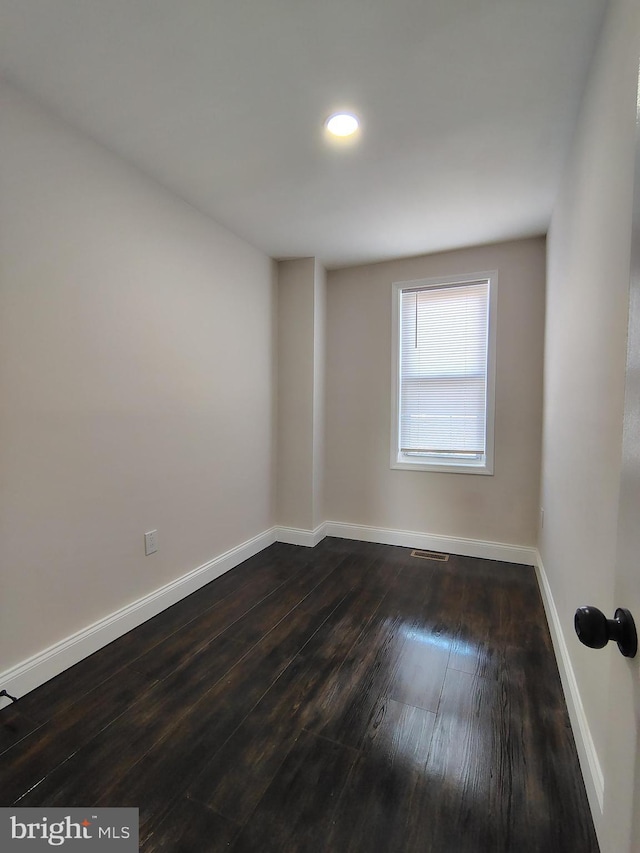 spare room featuring visible vents, baseboards, and dark wood-style flooring