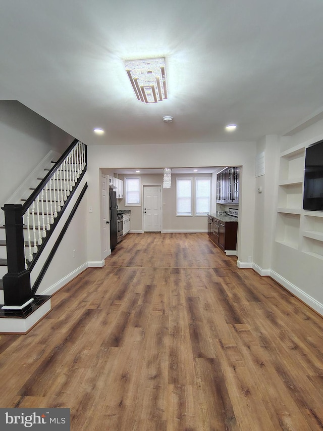 unfurnished living room with baseboards, built in features, stairs, recessed lighting, and wood finished floors