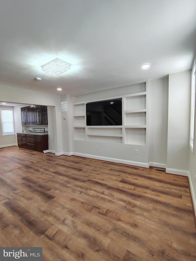 unfurnished living room featuring recessed lighting, baseboards, built in shelves, and dark wood-style flooring