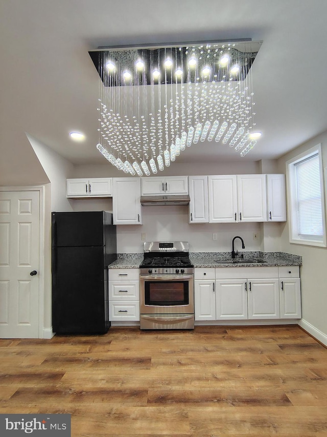 kitchen featuring under cabinet range hood, light wood-style flooring, stainless steel gas stove, and freestanding refrigerator