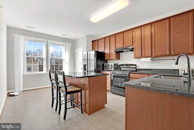 kitchen featuring stainless steel appliances, a kitchen island, dark stone counters, and sink