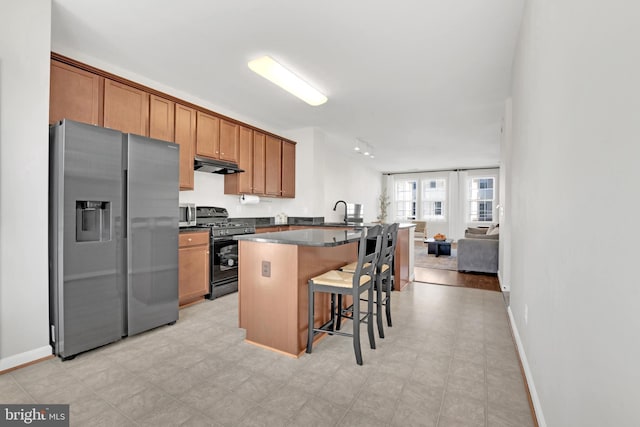 kitchen with a center island, sink, black gas range oven, a kitchen breakfast bar, and stainless steel fridge