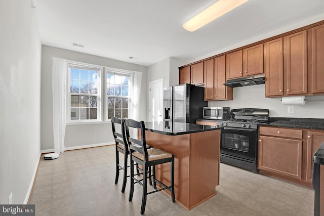 kitchen featuring a breakfast bar, a center island, black gas stove, dark stone countertops, and refrigerator with ice dispenser