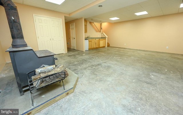 basement featuring a paneled ceiling, sink, and a wood stove