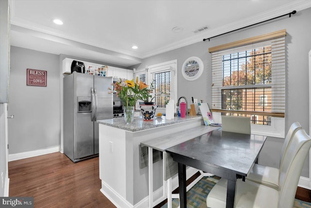 kitchen with kitchen peninsula, stainless steel refrigerator with ice dispenser, light stone countertops, crown molding, and dark wood-type flooring