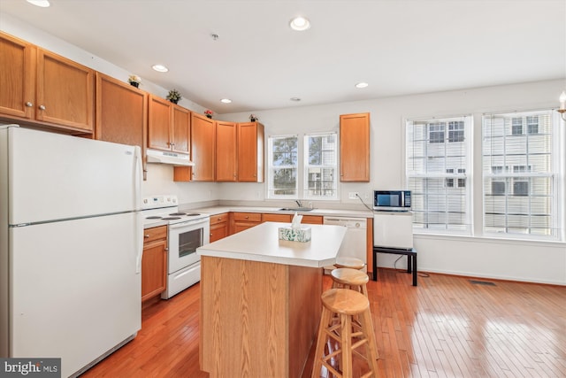 kitchen featuring a kitchen bar, white appliances, a center island, and light hardwood / wood-style flooring