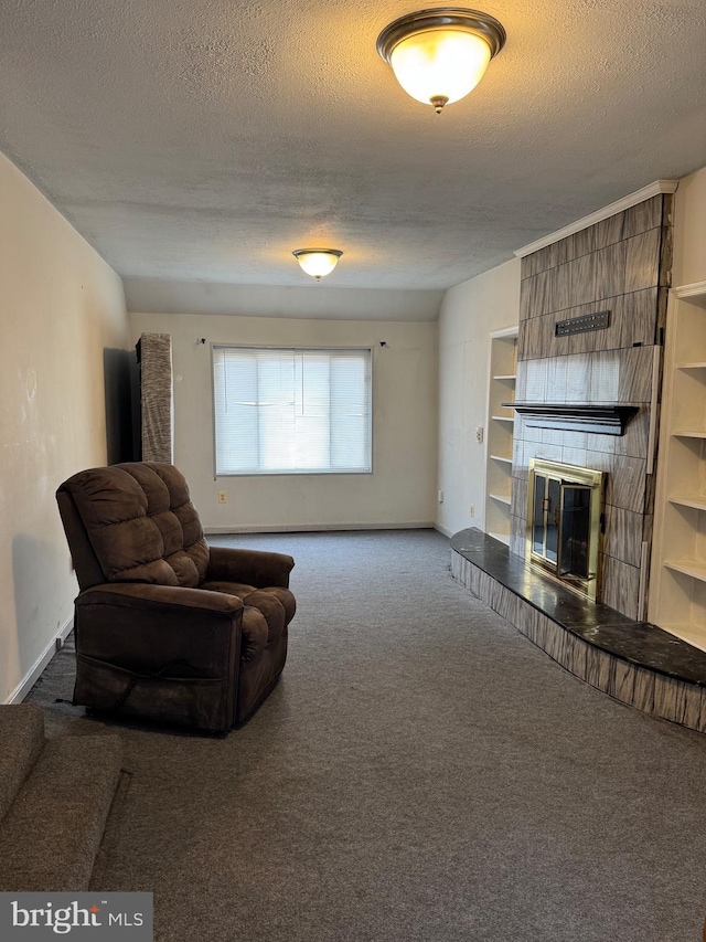 sitting room with carpet flooring, a tiled fireplace, built in shelves, and a textured ceiling