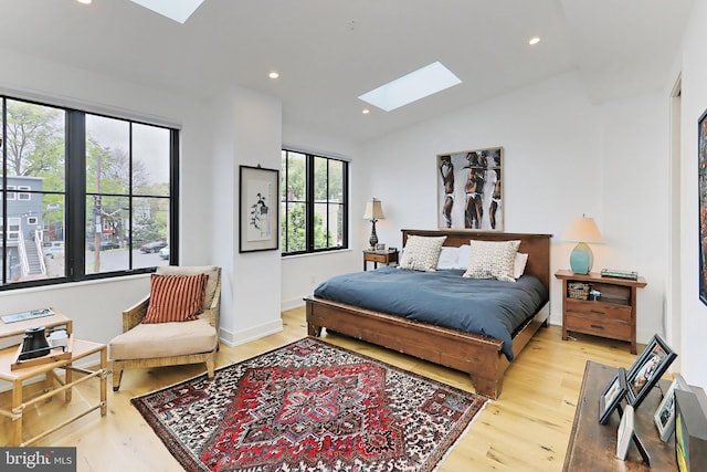 bedroom featuring multiple windows, lofted ceiling with skylight, and light hardwood / wood-style flooring