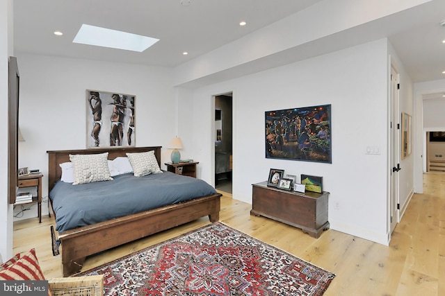 bedroom featuring a skylight, ensuite bathroom, and light hardwood / wood-style floors