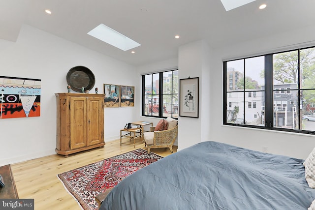 bedroom featuring multiple windows, lofted ceiling with skylight, and light hardwood / wood-style flooring