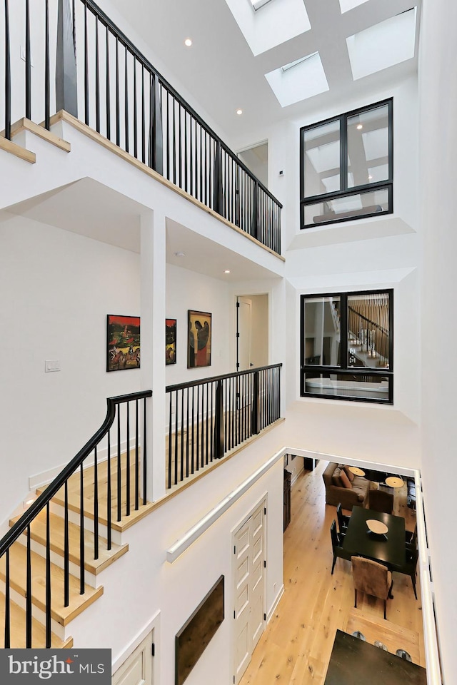 hallway featuring a skylight, light hardwood / wood-style flooring, and a towering ceiling