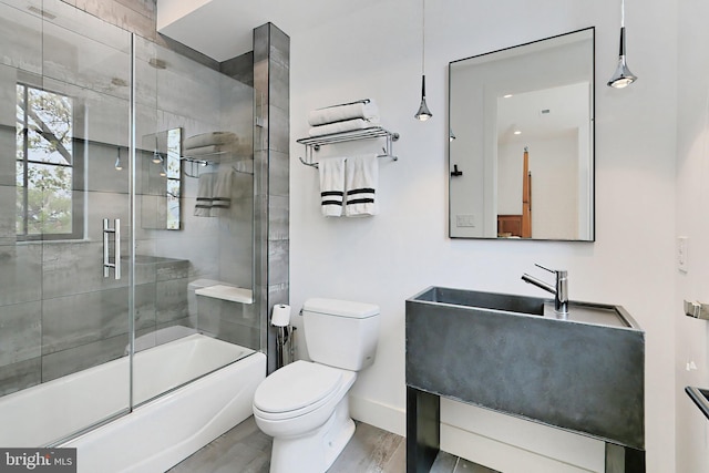 bathroom with hardwood / wood-style floors, bath / shower combo with glass door, and toilet